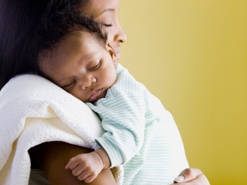 Bild einer Mutter, die ihr Baby sanft auf ihrer Schulter in den Schlaf wiegt