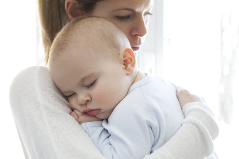 Das Bild einer Mutter, die ihr Baby auf ihrer Schulter in den Schlaf wiegt