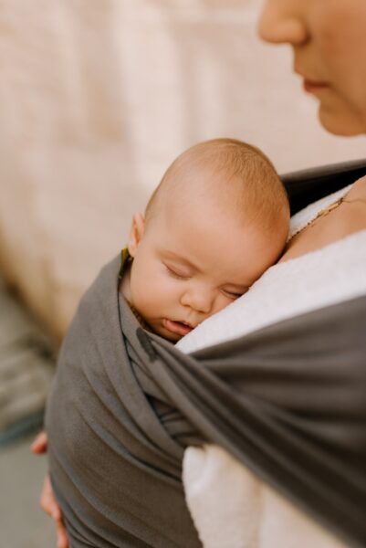 Bild einer Mutter, die ihr Baby mit einem Tragetuch in den Schlaf wiegt